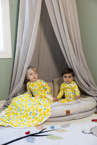 Two toddlers sitting in a crib wearing lemon patterned sleepwear